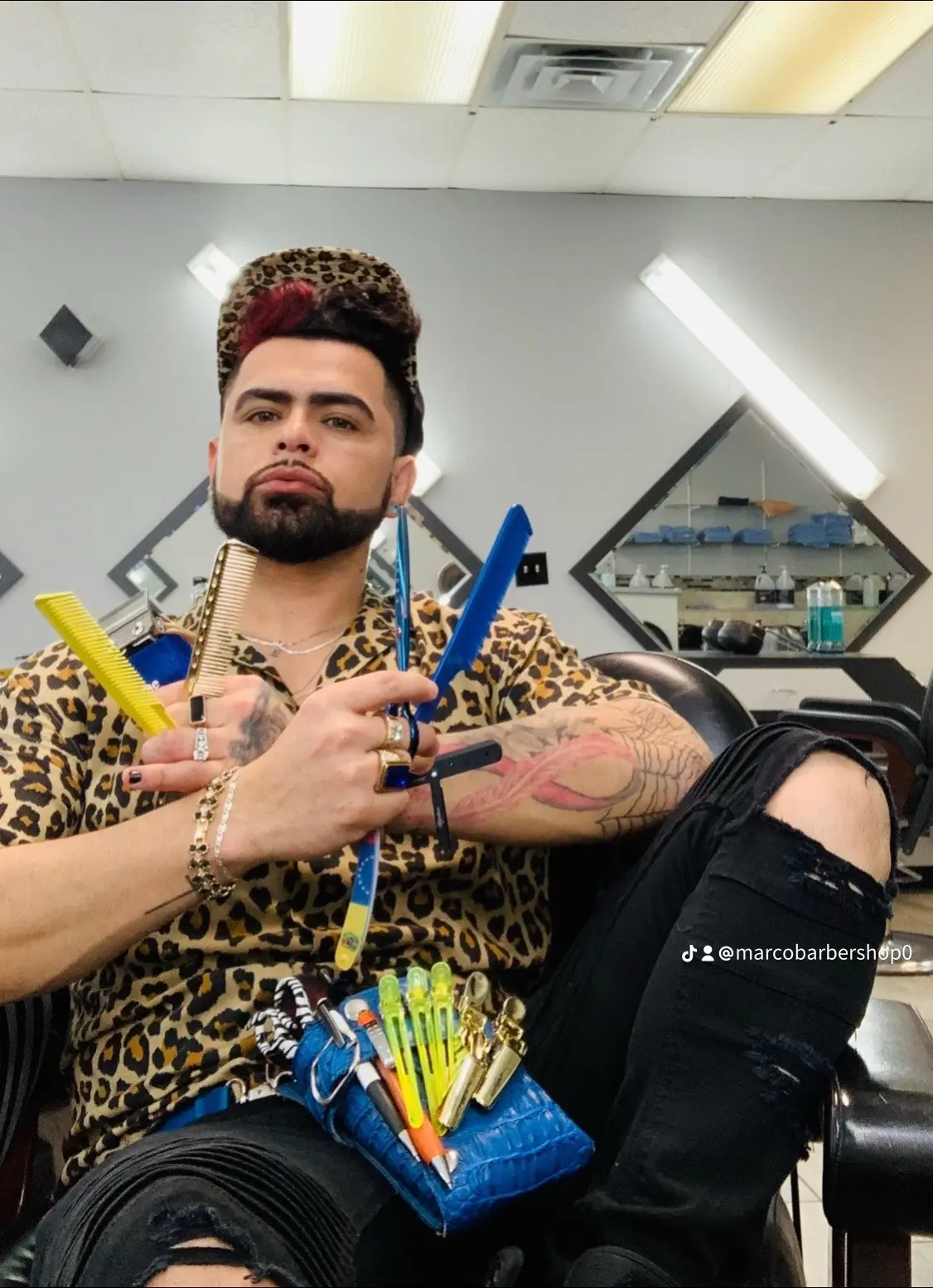 Jan-Marco en su silla de Vasti Barbershop, posando con tijeras, peines y navajas